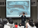 新幹線運転手の衣装で新幹線運転席の説明をする鈴木氏の様子です。